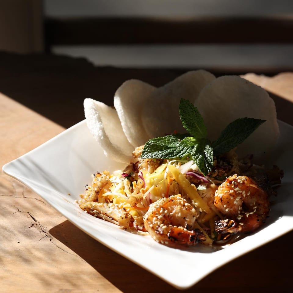 Vietnamese shrimp and mango salad with mint and rice crackers on a white plate.