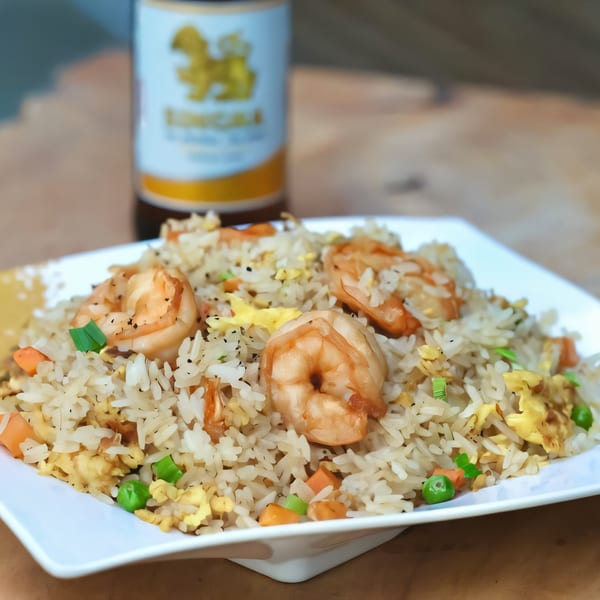 Shrimp fried rice with vegetables and egg on a white plate, with a beer bottle in the background.