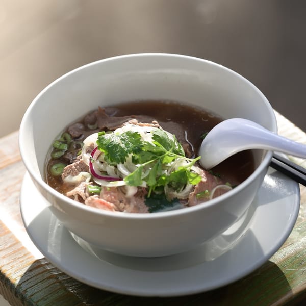 A bowl of Anh's Kitchen's Vietnamese pho with beef, onions, and cilantro, on a wooden table.