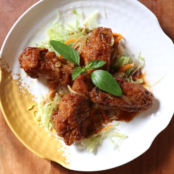 Four crispy, glazed chicken wings with basil, shredded lettuce, and carrots on a white plate.