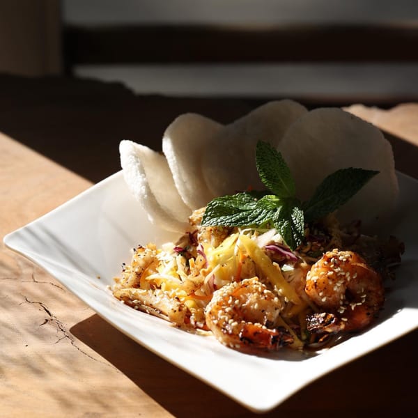 Vietnamese shrimp and mango salad with mint and rice crackers on a white plate.