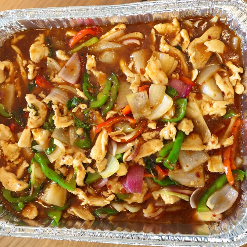 Chicken stir-fry with onions, green and red peppers in a savory sauce, served in a foil container.