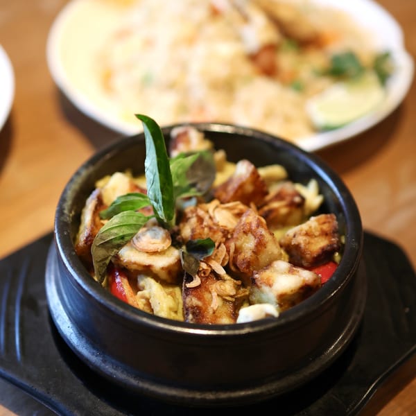 Close-up of a black bowl filled with green curry, fried tofu, and basil leaves.