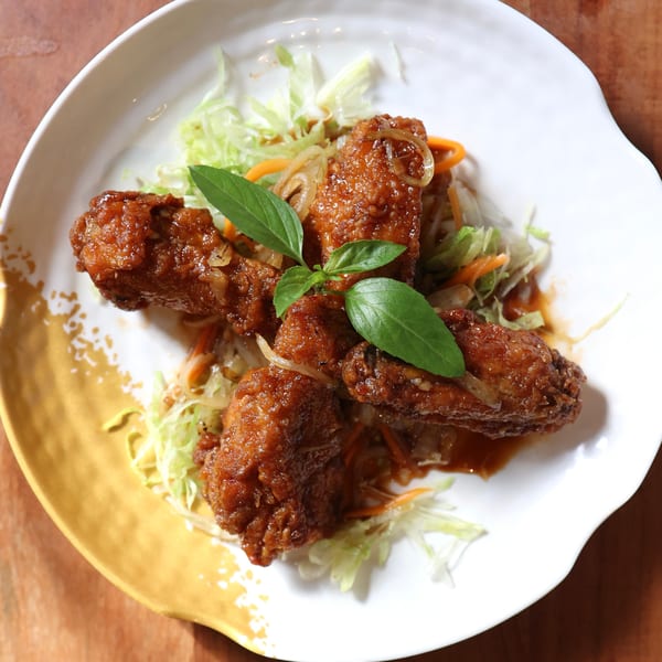 Crispy glazed chicken wings with shredded lettuce, carrots, onions, and basil on a white plate.