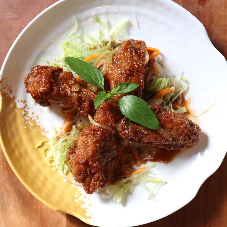 Crispy glazed chicken wings with shredded lettuce, carrots, onions, and basil on a white plate.