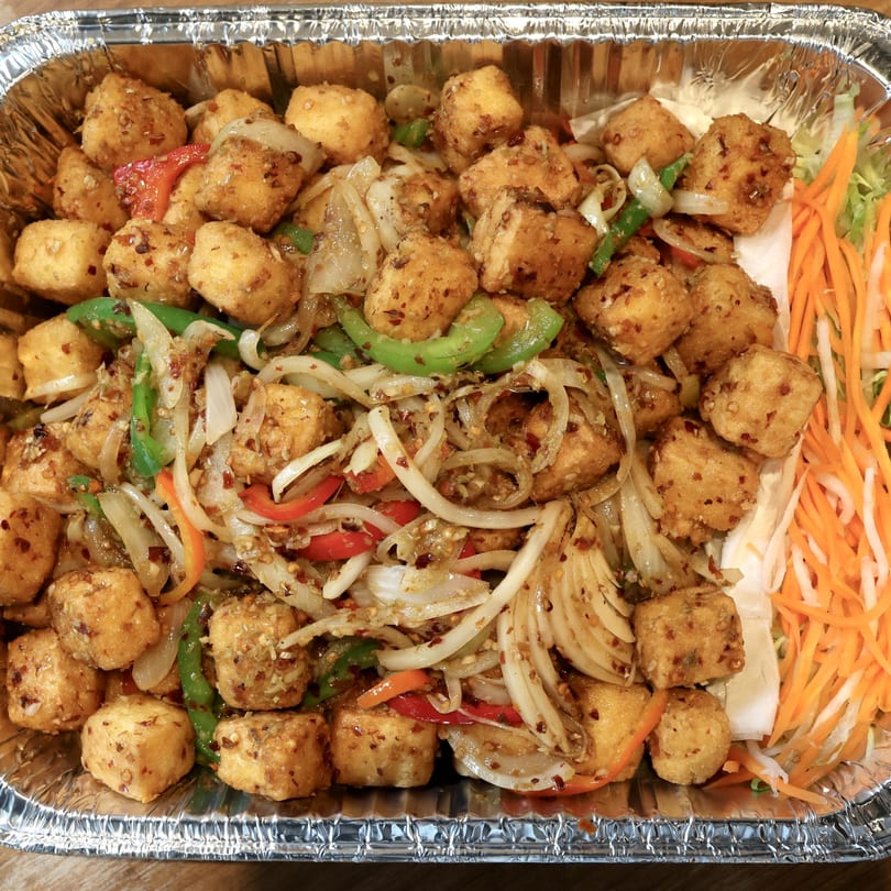 Crispy tofu with stir-fried onions, peppers, and shredded carrots in a foil takeout container.