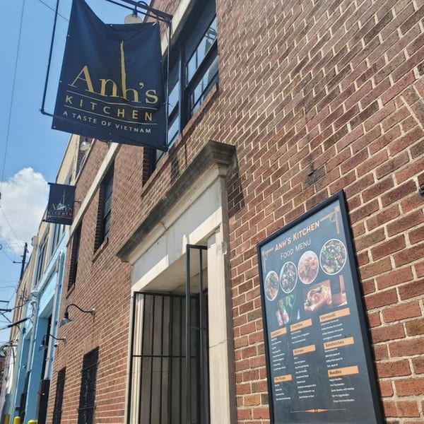 Anh's Kitchen sign and outdoor menu board on a brick building facade under a blue sky.