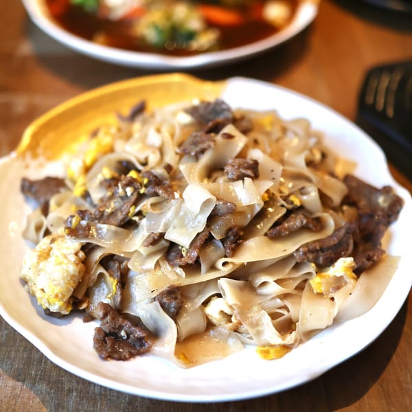 Close-up of a white plate filled with wide rice noodles, beef, and scrambled egg.