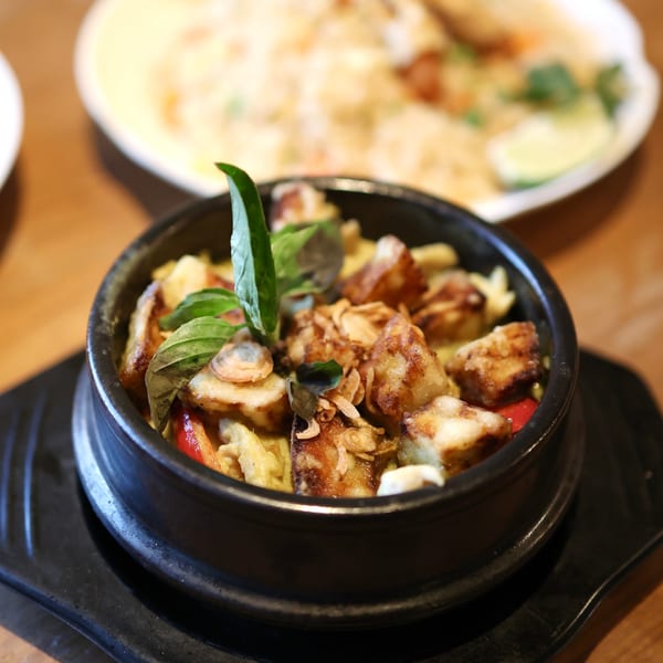 A black bowl of Thai green curry with fried tofu, basil, and crispy shallots.